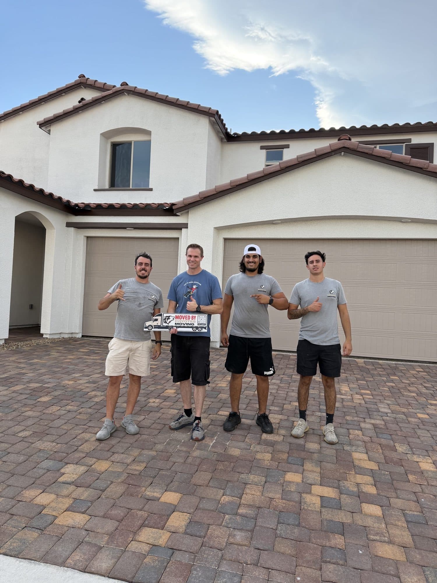 Coyotes Moving customers holding the "Moved By Coyotes Moving" sign in front of their new home