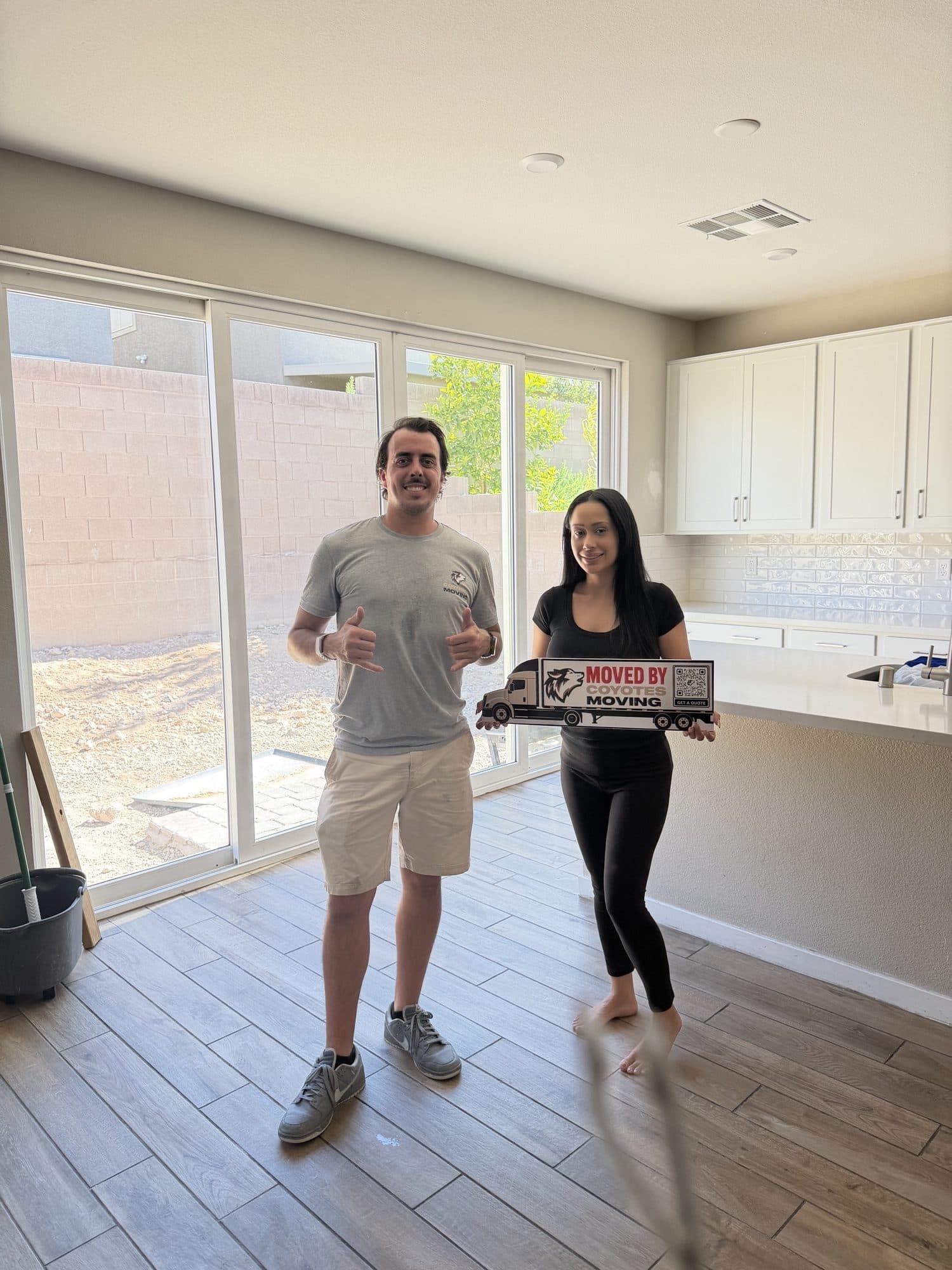 Coyotes Moving customers holding the "Moved By Coyotes Moving" sign in their new kitchen