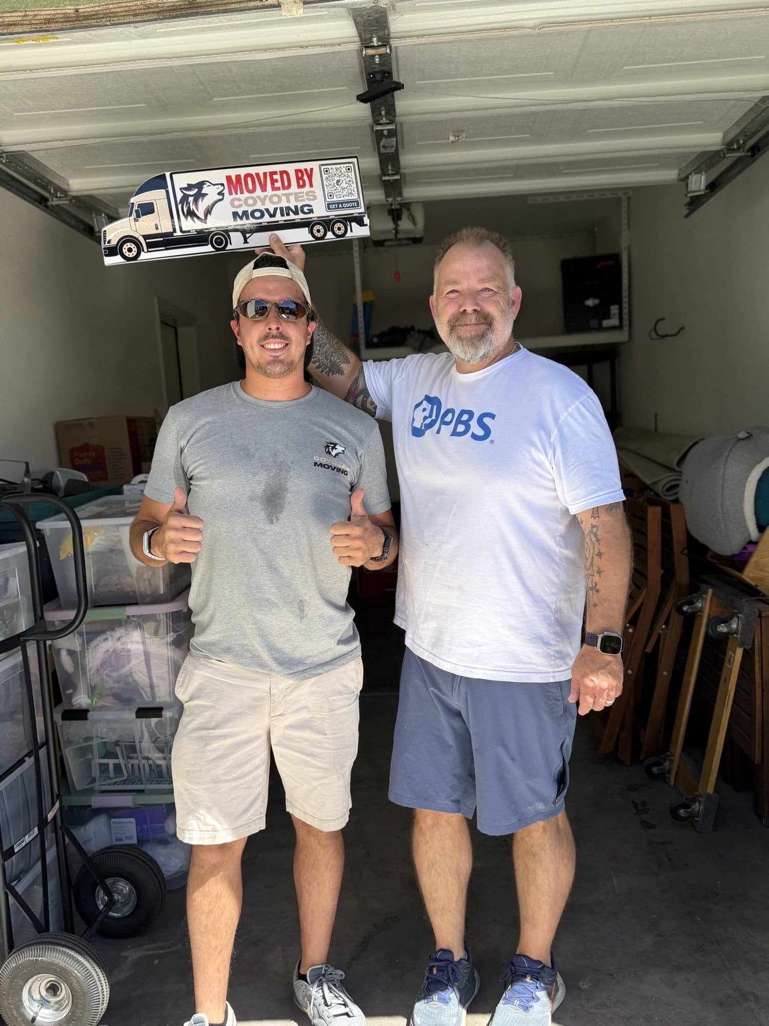 Coyotes Moving customers holding the "Moved By Coyotes Moving" sign in the garage