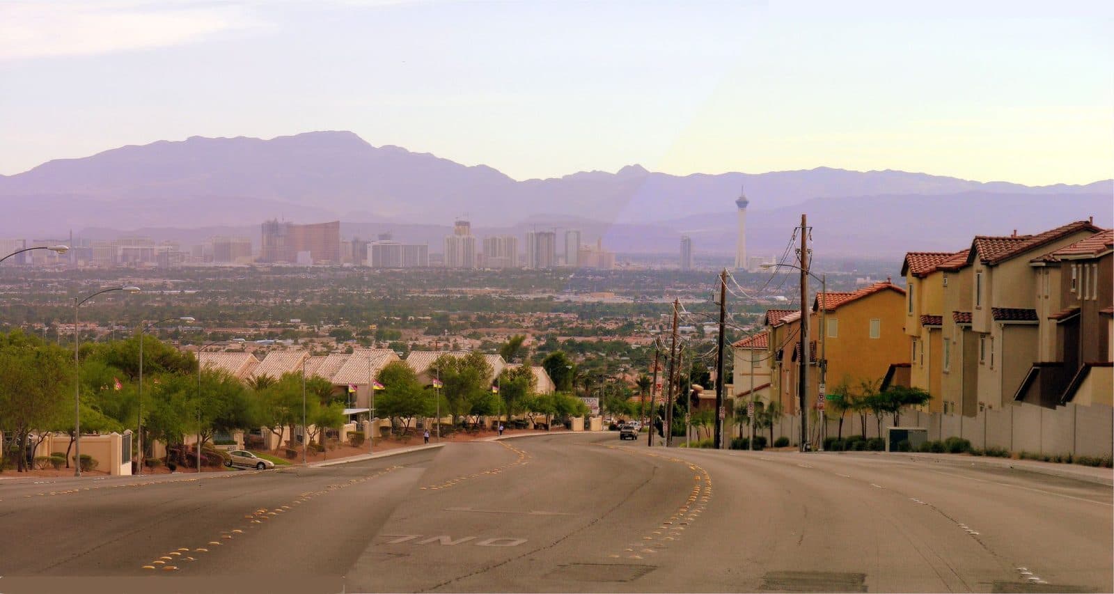 Residential street in North Las Vegas lined with houses, with the Strip skyline in the distance